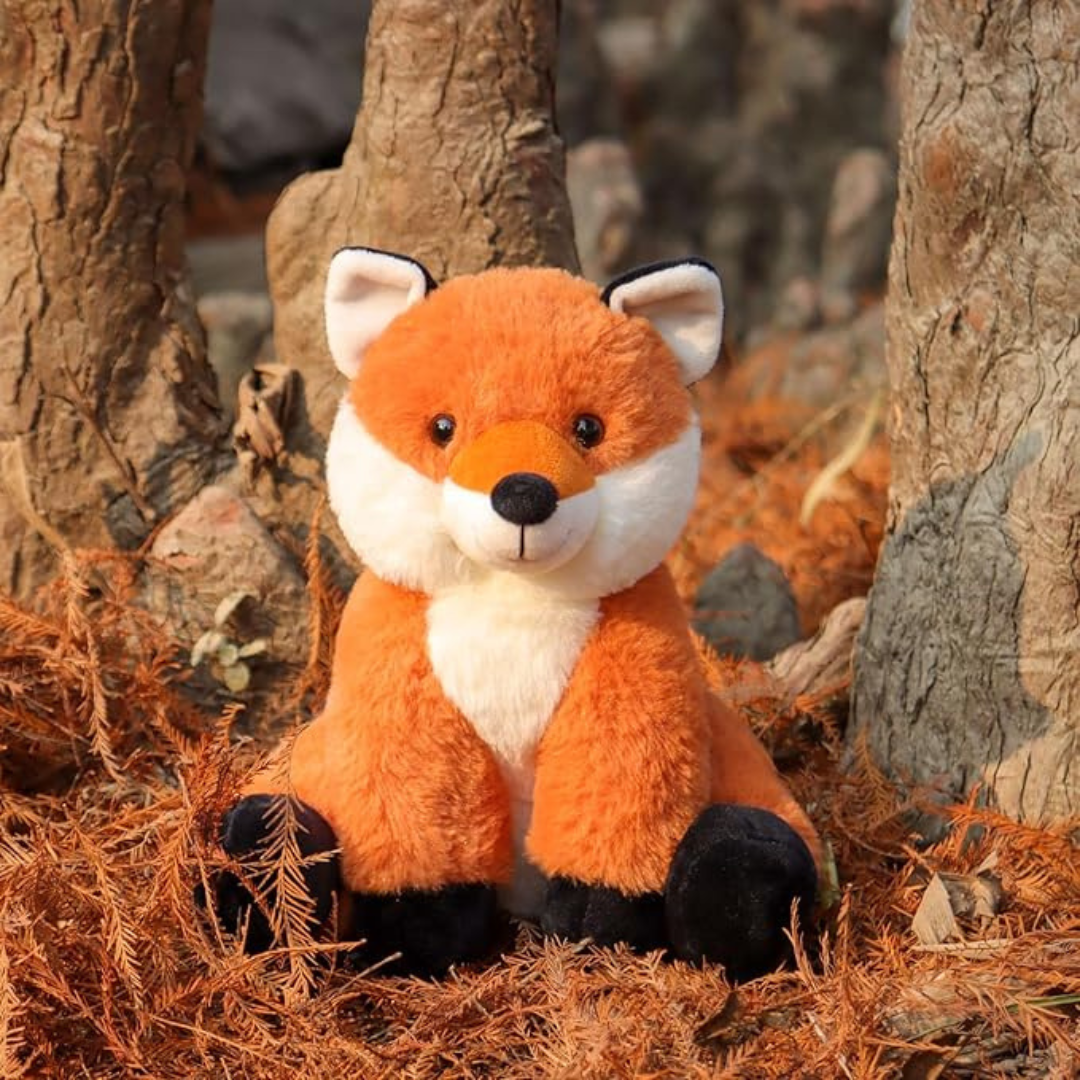 Plush fox toy in a natural setting with trees and foliage.
