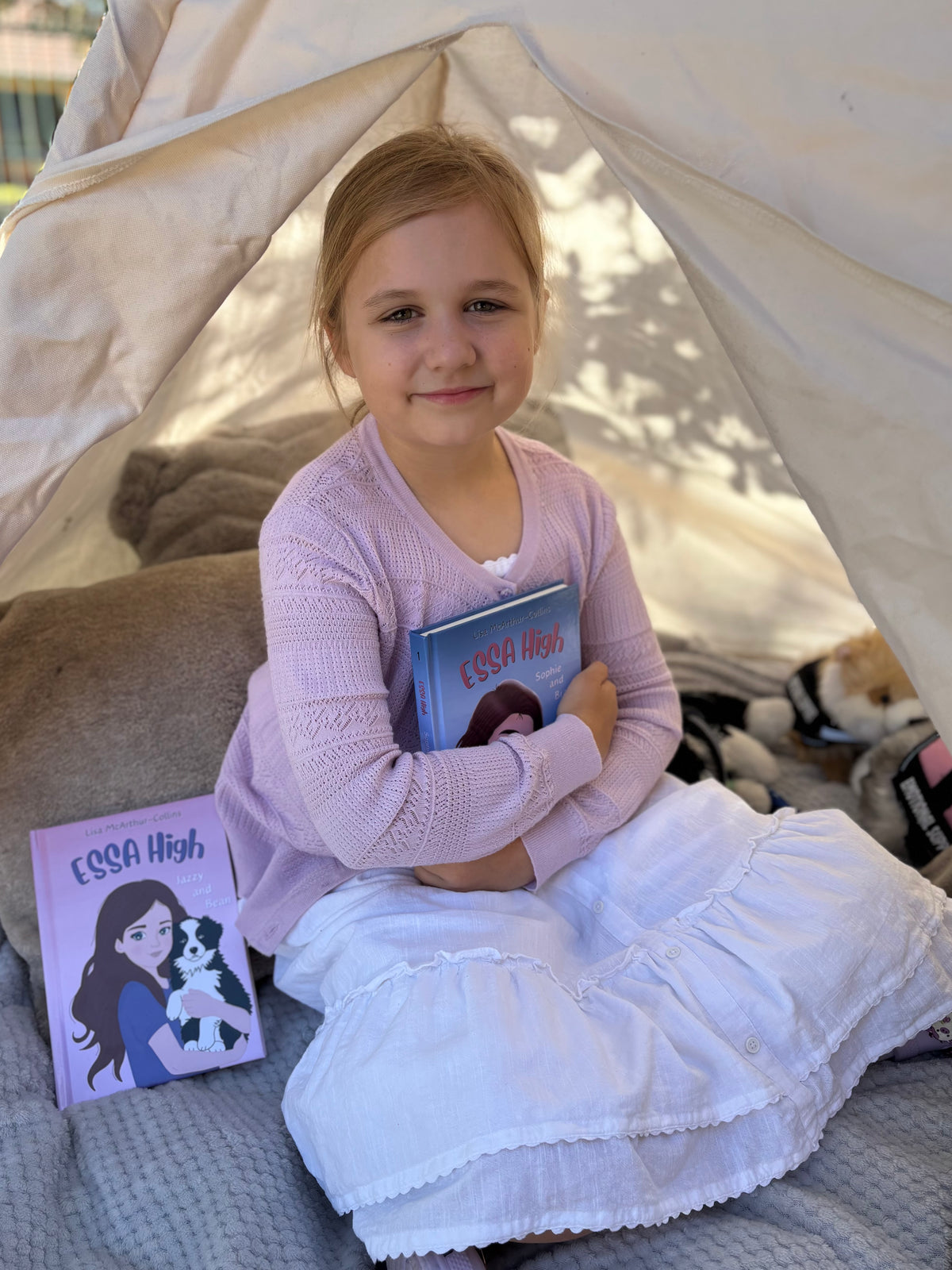 Young girl holding a book inside a tent with a 'Elsa High' book on a surface next to her.