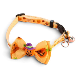 A pet collar with a large orange bow featuring a jack-o'-lantern pattern, a small purple witch hat charm, and a rose gold bell on a white background.