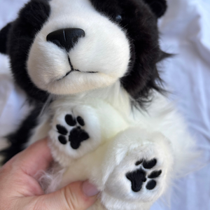 Close-up of a plush toy resembling a black and white animal, possibly a dog or cat, held by a hand.