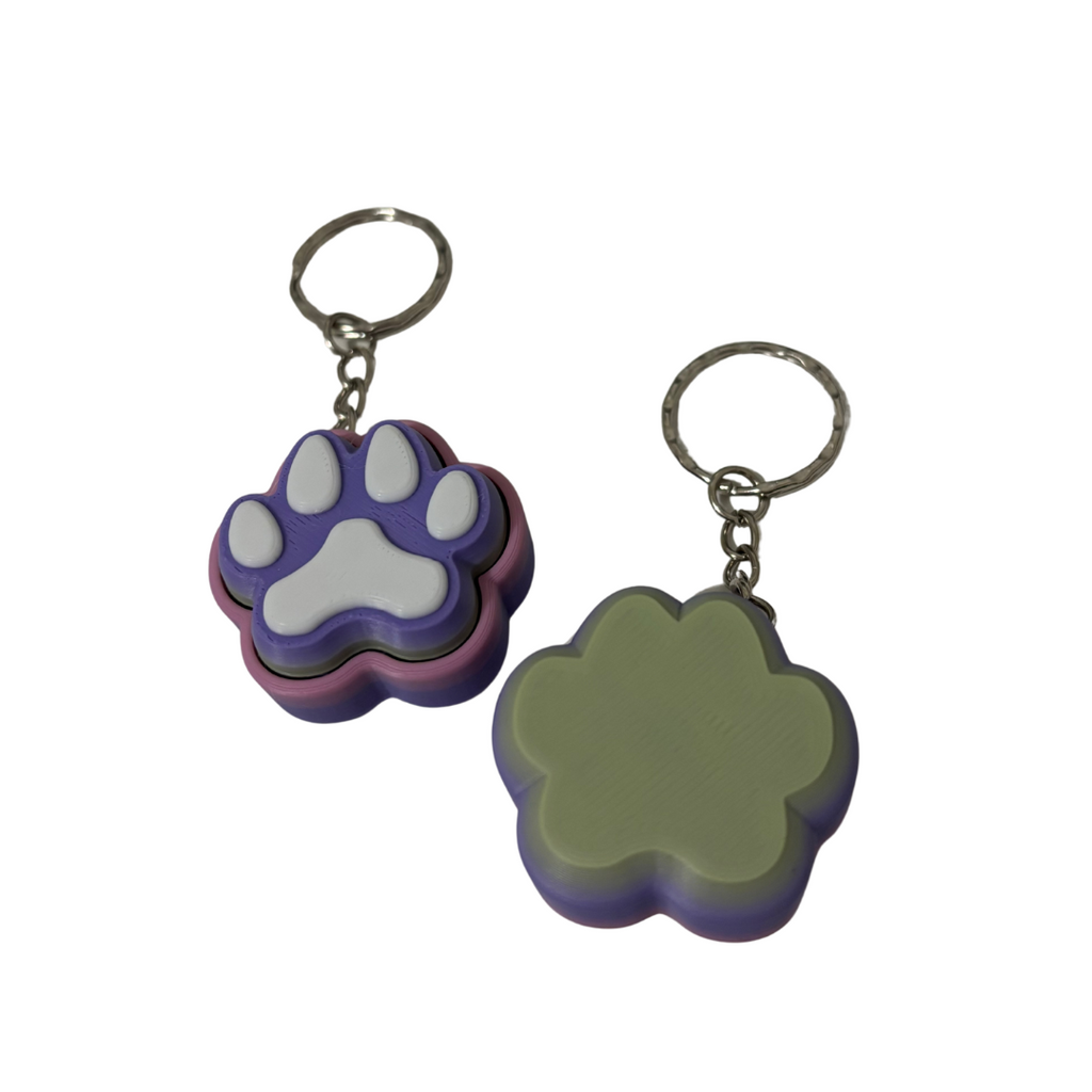 Two paw-shaped keychains, one purple and white, the other green and purple, on a white background.