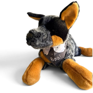A plush dog toy styled like a black and tan dog, lying down and wearing a dark bandana that says 'Boo!'.
