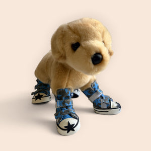 A plush golden retriever toy wearing blue and white canvas-style booties with black star details, photographed against a plain warm beige background.