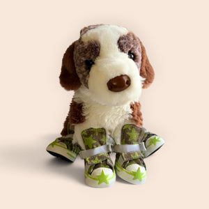 A plush dog toy wearing camouflage booties with green star details, photographed against a solid pale peach background.