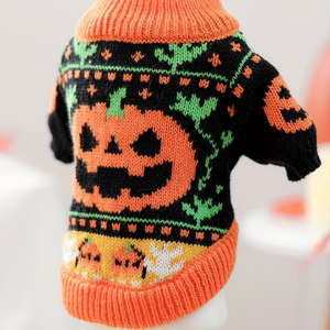 A close-up of a knitted pet sweater with a Halloween theme, featuring a large orange jack-o'-lantern on a black background with green leaf patterns and orange trim.