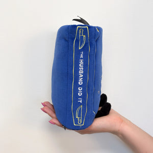 Blue pouch with 'The Husband Did It' text held by a hand on a white background