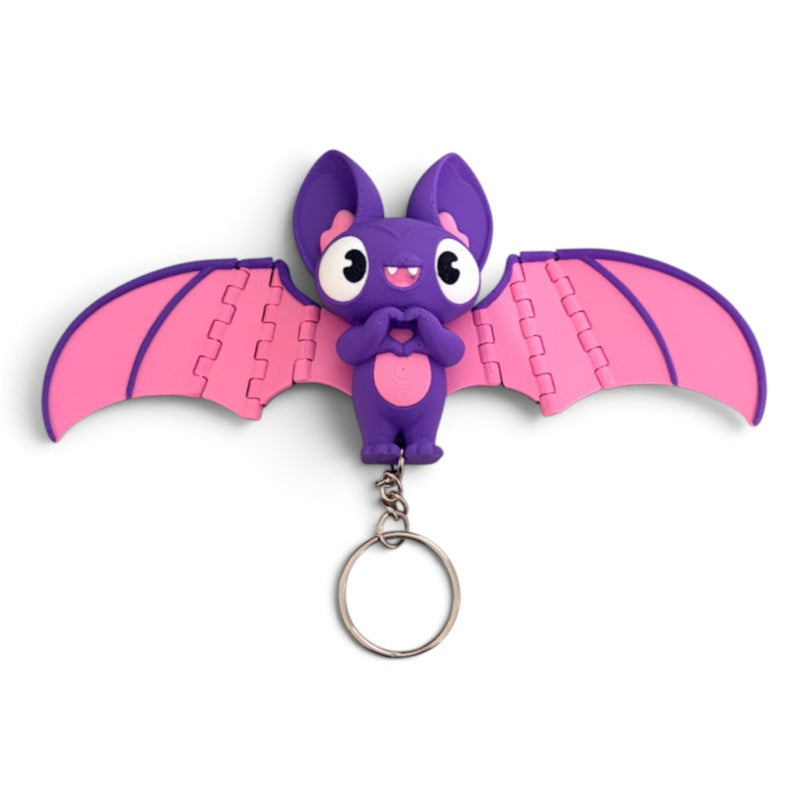 A purple and pink bat-shaped keychain charm with large cartoon eyes, a small metal key ring, and wing puzzle-piece details, shown on a plain white background.