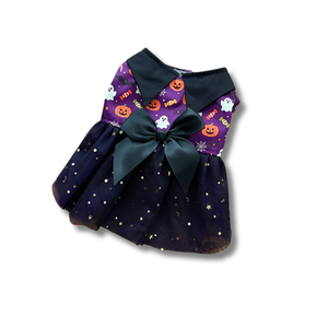 A small Halloween-themed pet dress with a dark navy blue tulle skirt decorated with gold stars, a purple collar panel with orange jack-o'-lanterns and white ghosts, and a large dark green satin bow at the center.