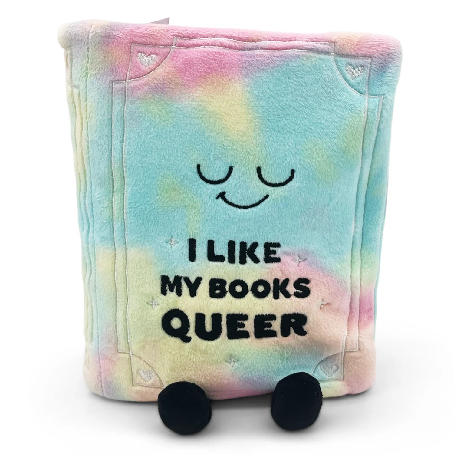 A plush book-shaped pillow with a pastel tie-dye pattern in pink, blue, yellow, and green. It features embroidered black eyes and a smiley face, with the text 'I LIKE MY BOOKS QUEER' printed in black.