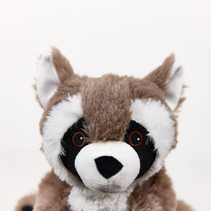 A close-up of a plush raccoon toy against a plain white background. The raccoon has brown and white fur with black around its eyes and a white snout, and small orange-rimmed eyes.