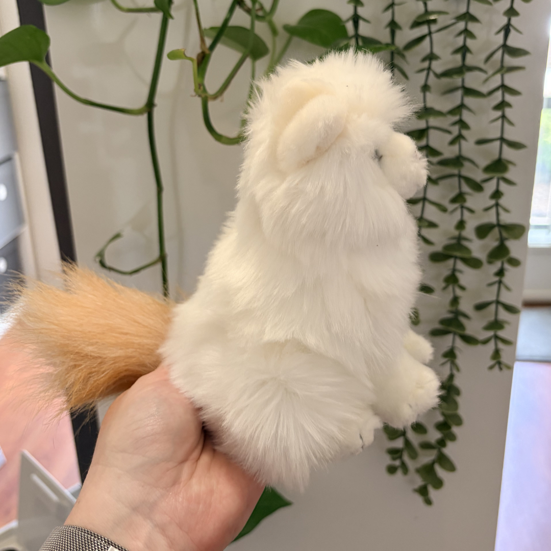 White fluffy toy held in a hand with green plants in the background