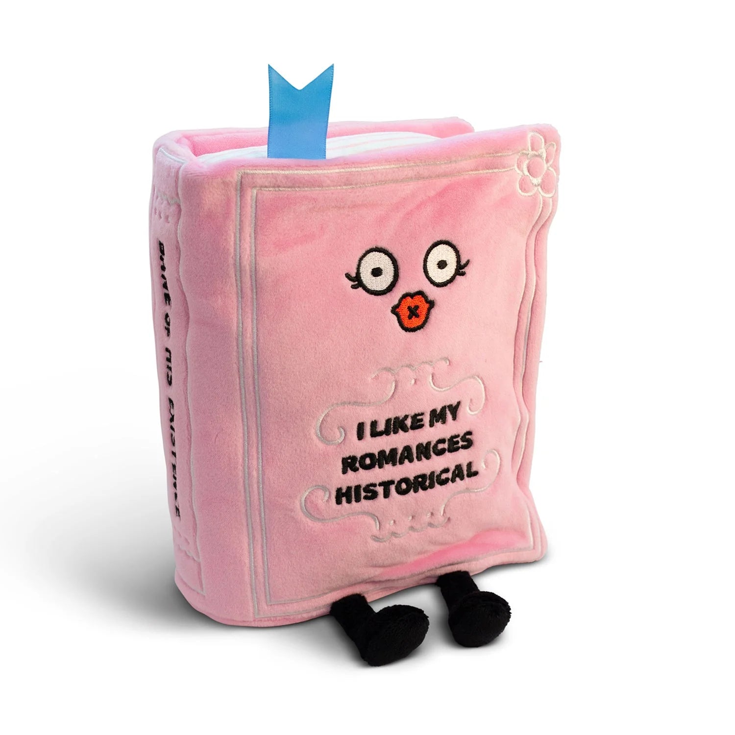 A pink plush book-shaped pillow with embroidered eyes, a small orange mouth, and the text 'I LIKE MY ROMANCES HISTORICAL' on the front, with black feet and a blue bookmark tab sticking out, photographed on a white background.