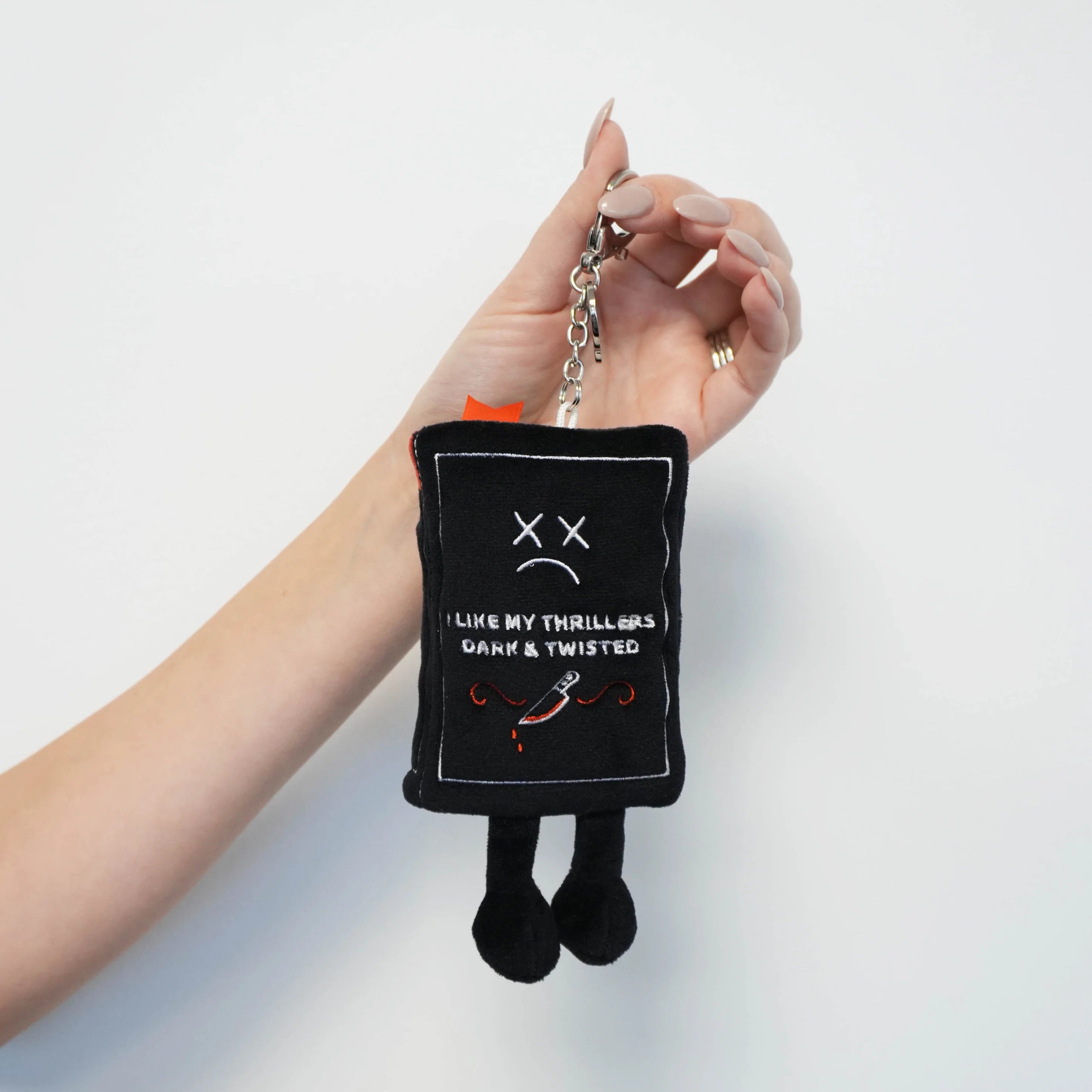 Black plush keychain with text and a sad face held by a hand against a white background