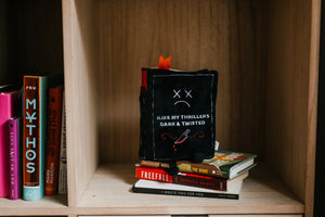 Stack of books with a plush toy resembling a face on a wooden shelf