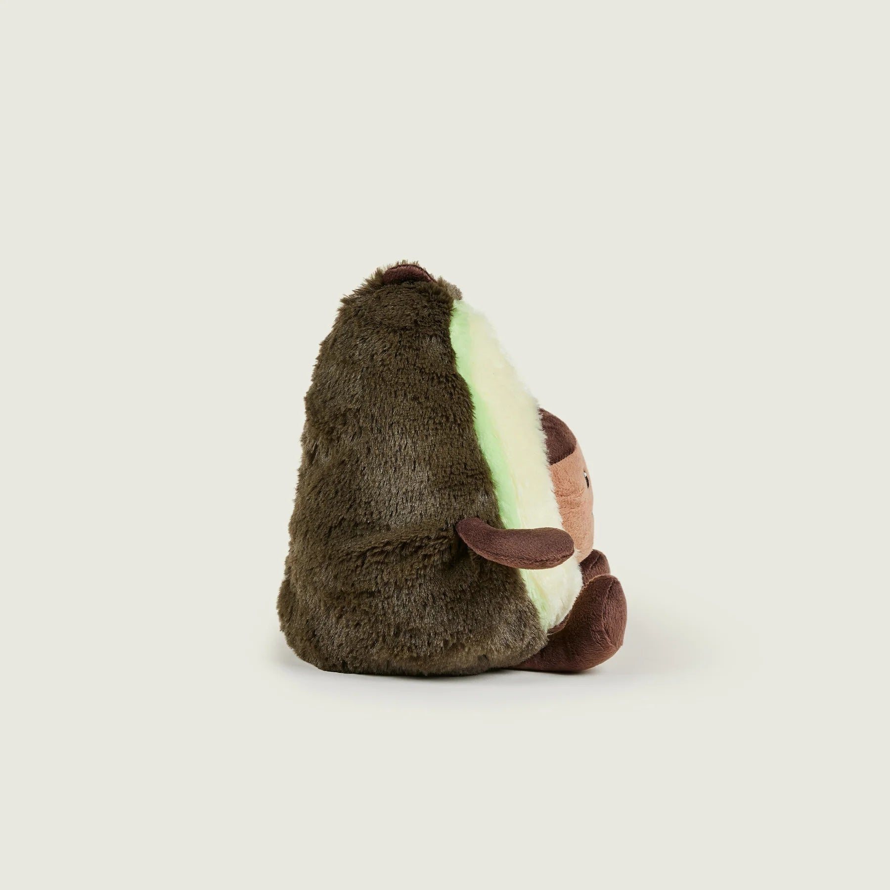 A plush avocado toy shown from the back, featuring dark brown fuzzy outer skin, a cream-colored inner flesh side with a glowing mint green light, and small brown eyes and nose details, set against a solid light gray background.