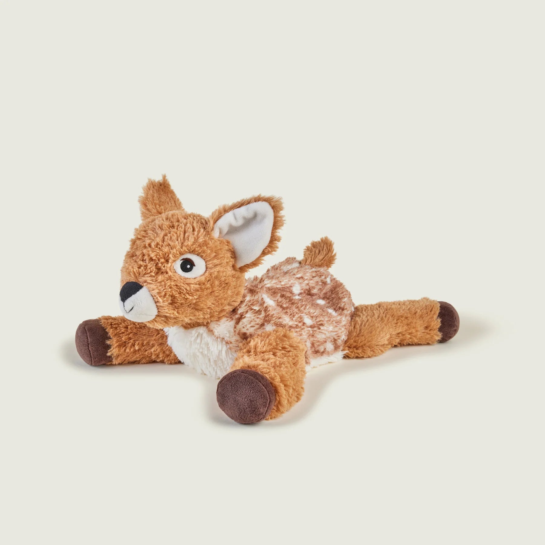 A plush stuffed deer toy lying on its side, made of soft brown and white faux fur with dark brown hooves and a white muzzle, photographed on a plain light beige background.