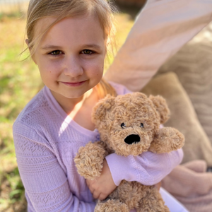 Girl holding a Bear plushie - Warmies brand - weighted, lavender scented heat bag 