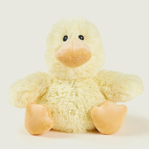 A small plush yellow duck toy with a soft fuzzy body, peach-colored beak and feet, and black bead eyes, photographed against a light warm gray background.