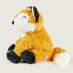 A plush toy fox sitting down, featuring orange fur, a white muzzle and tail tip, and black paws and ears, photographed against a solid light beige background.