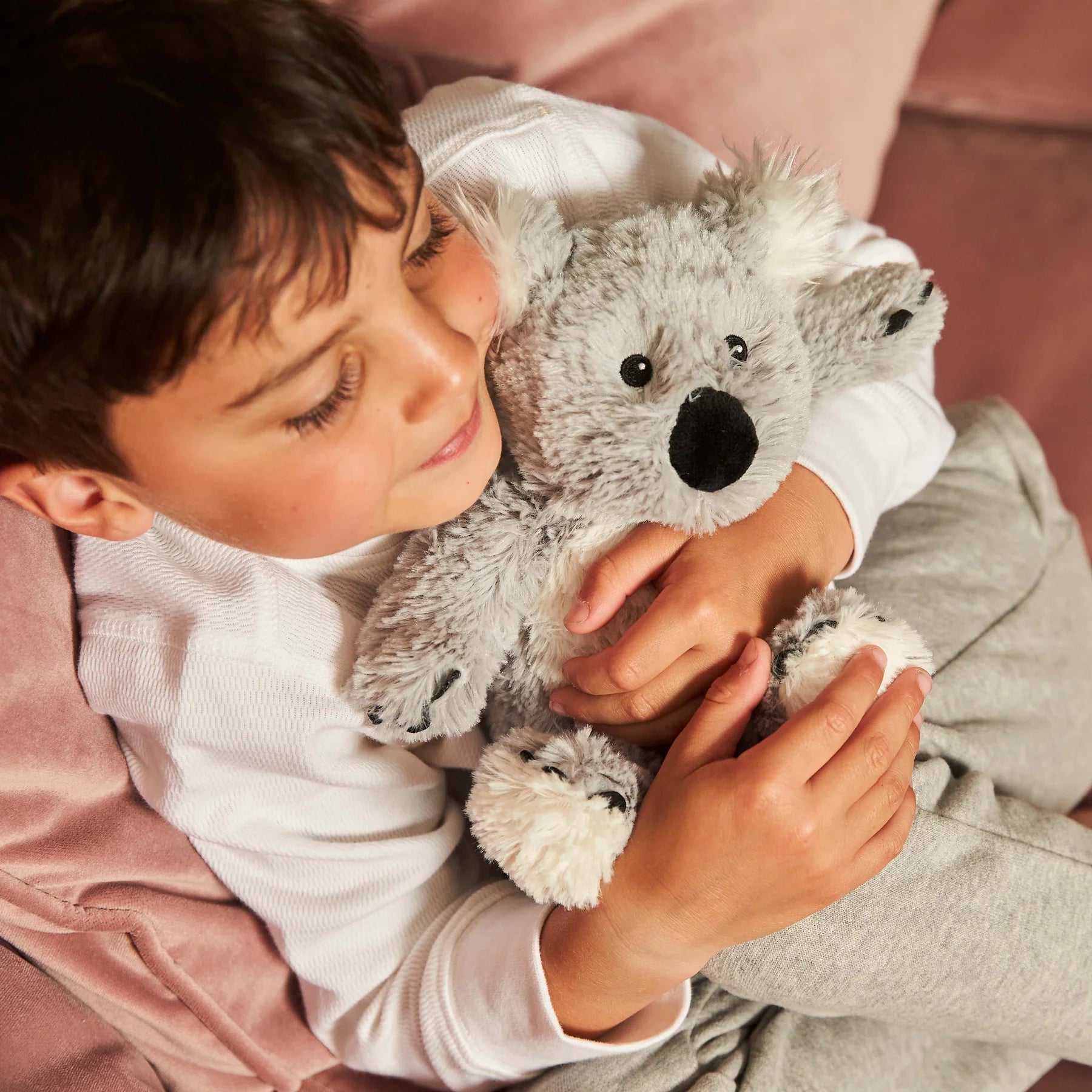 Child holding a plush koala toy on a pink blanket