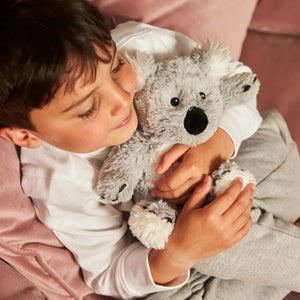 Child holding a plush koala toy on a pink blanket