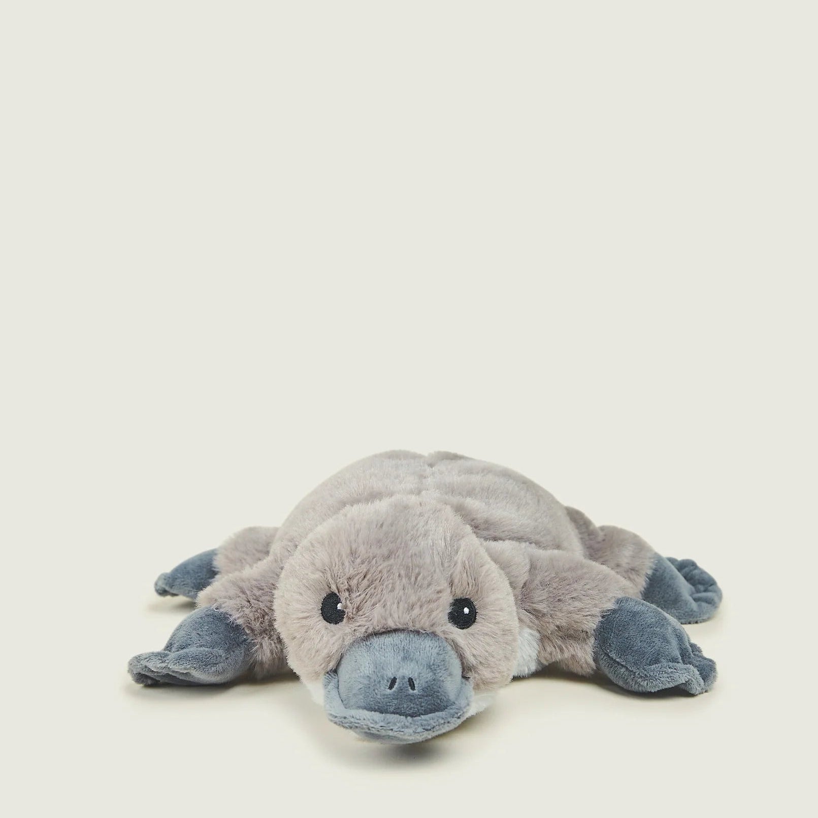 A plush stuffed animal of a platyptodont (platyptodon) toy, featuring a soft gray body and blue-gray snout, feet, and hands, lying on its side against a light cream background.