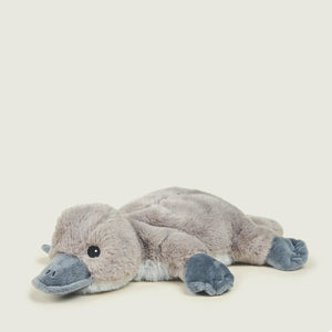 A plush stuffed animal shaped like a platypus, lying on its side. The toy is made of soft gray plush fabric with a darker gray beak, feet, and eye, and is photographed on a plain light beige background with rounded corners.