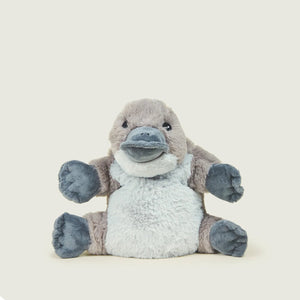 A plush toy of a sitting platypus, featuring a light gray fuzzy body, brownish-gray head and arms, and dark gray paws and beak, set against a solid cream-colored background with rounded corners.