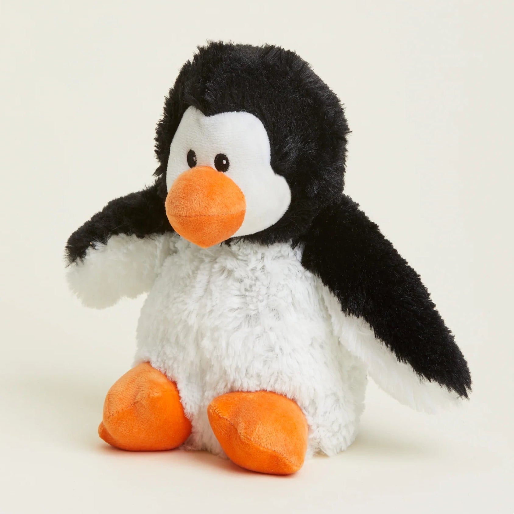 A plush penguin toy with black and white fur, a bright orange beak, and orange feet, sitting against a light cream background.