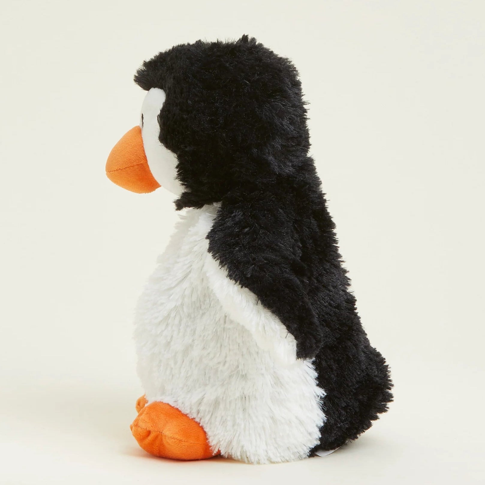 A plush penguin toy with black and white fur, an orange beak, and orange feet, shown from the side against a plain light background.