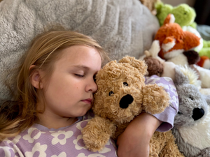 Girl holding a Bear plushie while asleep - Warmies brand - weighted, lavender scented heat bag - emotional regulation