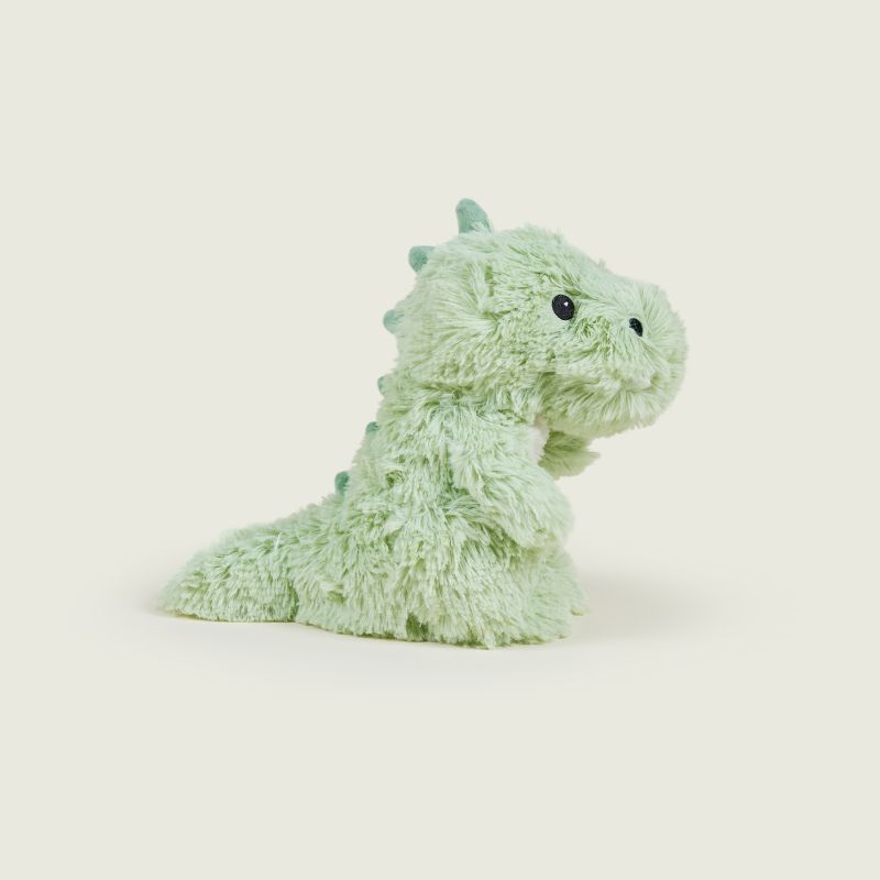 A light mint green plush dinosaur toy with small black bead eyes, photographed on a clean, solid, warm off-white background.