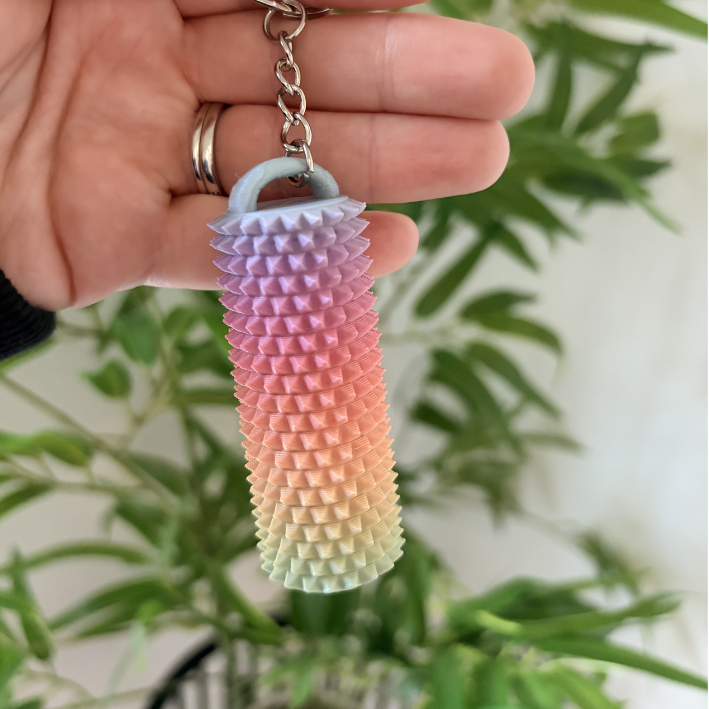 Colorful textured keychain held by a hand with a plant in the background