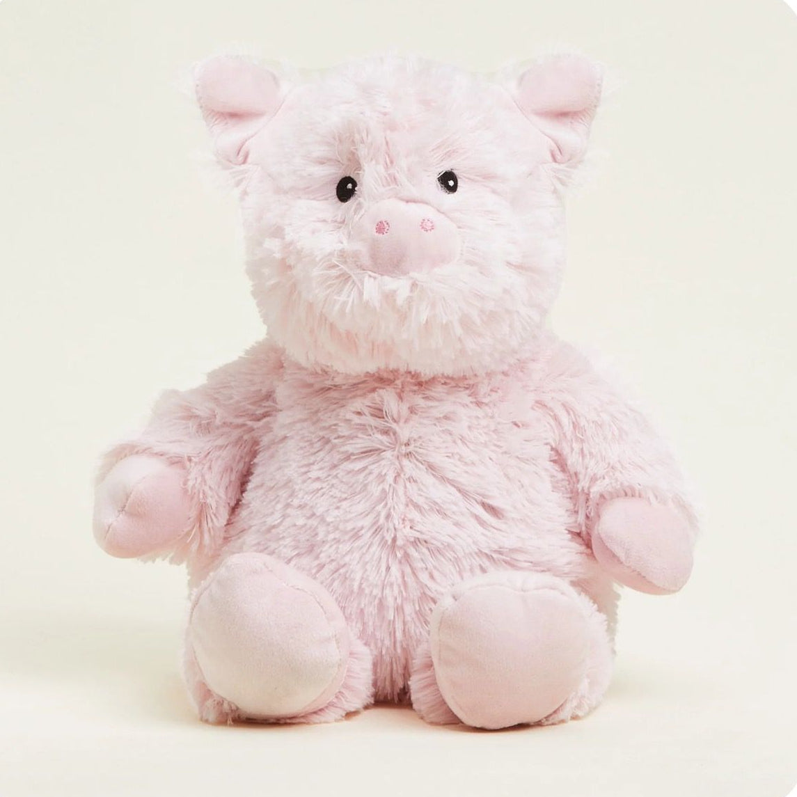 A soft pink plush pig toy with a fluffy texture, black bead eyes, and a pink snout, sitting against a light cream background.